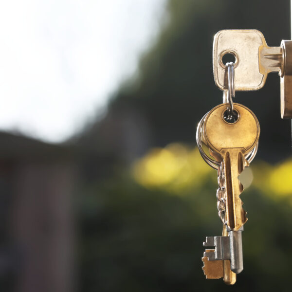 House keys in lock of a door viewed outside with soft glow background from natural lighting. Room for text. This image is also available in vertical orientation